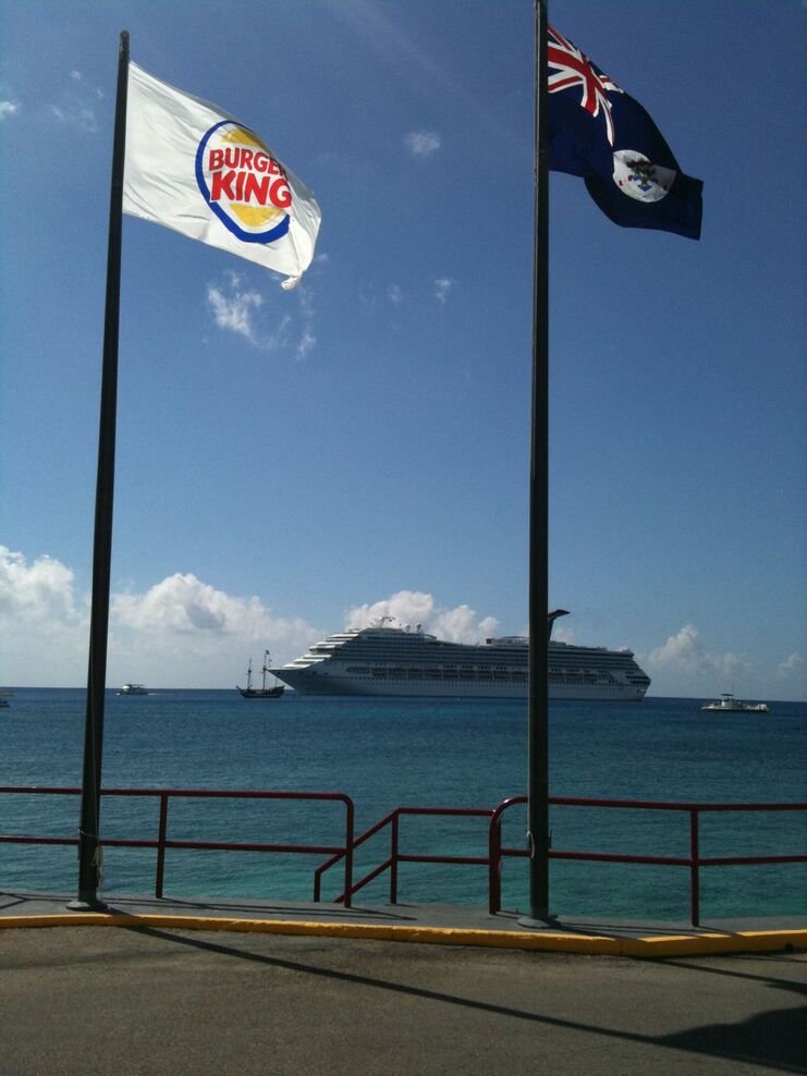 picture of the burger king flag an cayman islands flag with cruise ship in the background