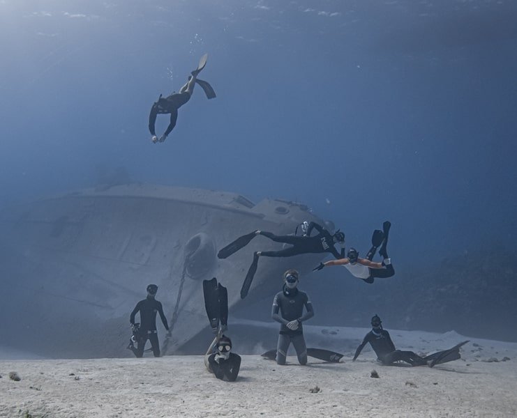 picture of 8 people on the seafloor underwater with shipwreck in background